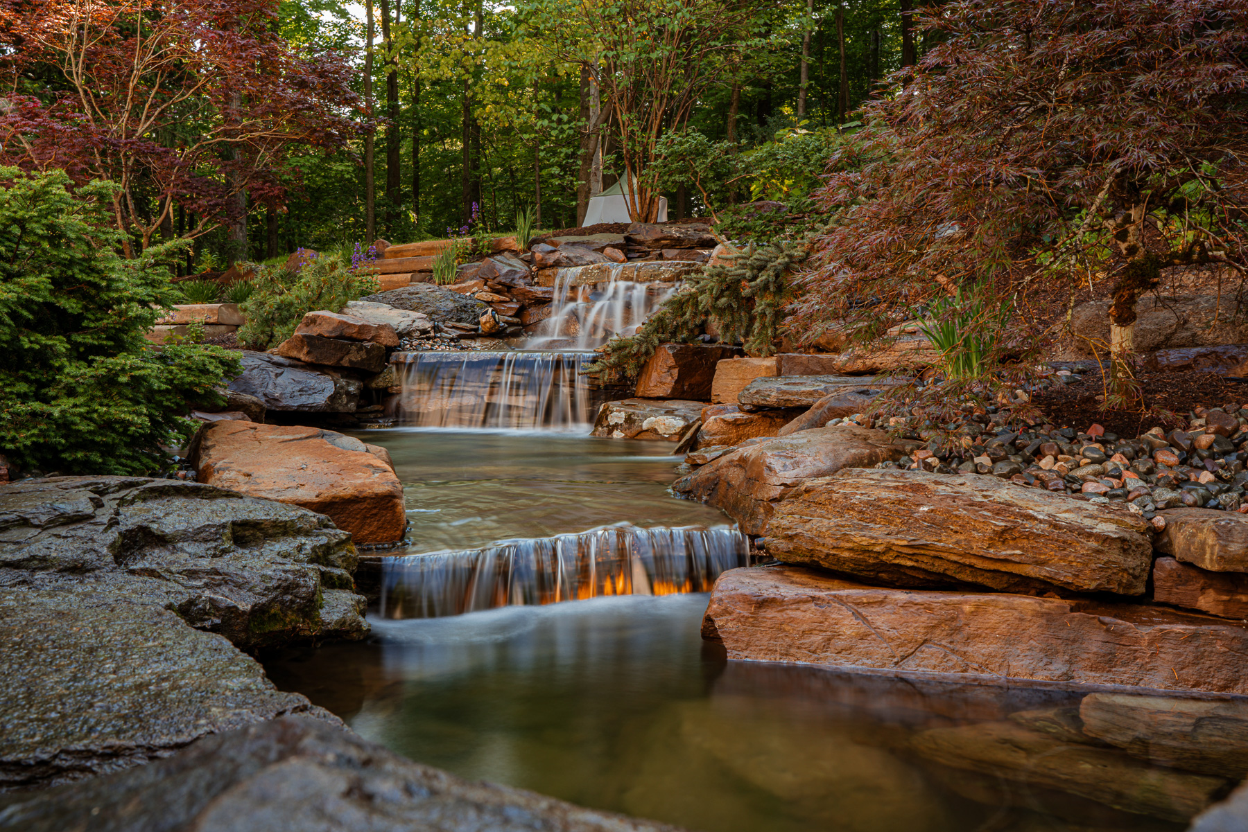 Cascading backyard waterfall built with natural boulders in a wooded Chagrin Falls landscape.